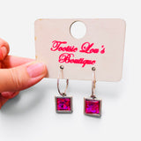 Faceted hot pink square crystal drop earrings suspended from polished silver-tone hoops.