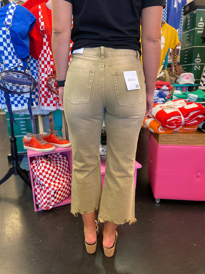 Back side of Light camel colored jeans with cropped length and distressing at knees. Raw hem line.