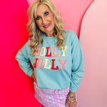 Light blue pullover with pink and white accents and gold sequin-trimmed “Holly Jolly” patches.