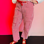 Red striped twill barrel-leg pants with rope tie, silver eyelets, and decorative pockets made from cotton.