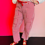 Red striped twill barrel-leg pants with rope tie, silver eyelets, and decorative pockets made from cotton.