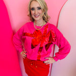 Pink sweatshirt with red sequin bow design, cozy fit, and festive holiday style.