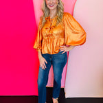 Orange metallic peplum top with bow pattern, U-neckline, and three-quarter balloon sleeves.