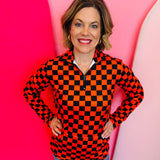 Orange and black checkered pullover with collared neckline, quarter-zip front, and kangaroo pocket, laid flat to show pattern and structure.