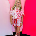 Full body view of a woman wearing the Cherry Bomb Ruffle Pajama Set, showcasing the matching cherry print top and ruffle shorts with a decorative tie