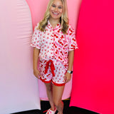 Full body view of a woman wearing the Cherry Bomb Ruffle Pajama Set, showcasing the matching cherry print top and ruffle shorts with a decorative tie