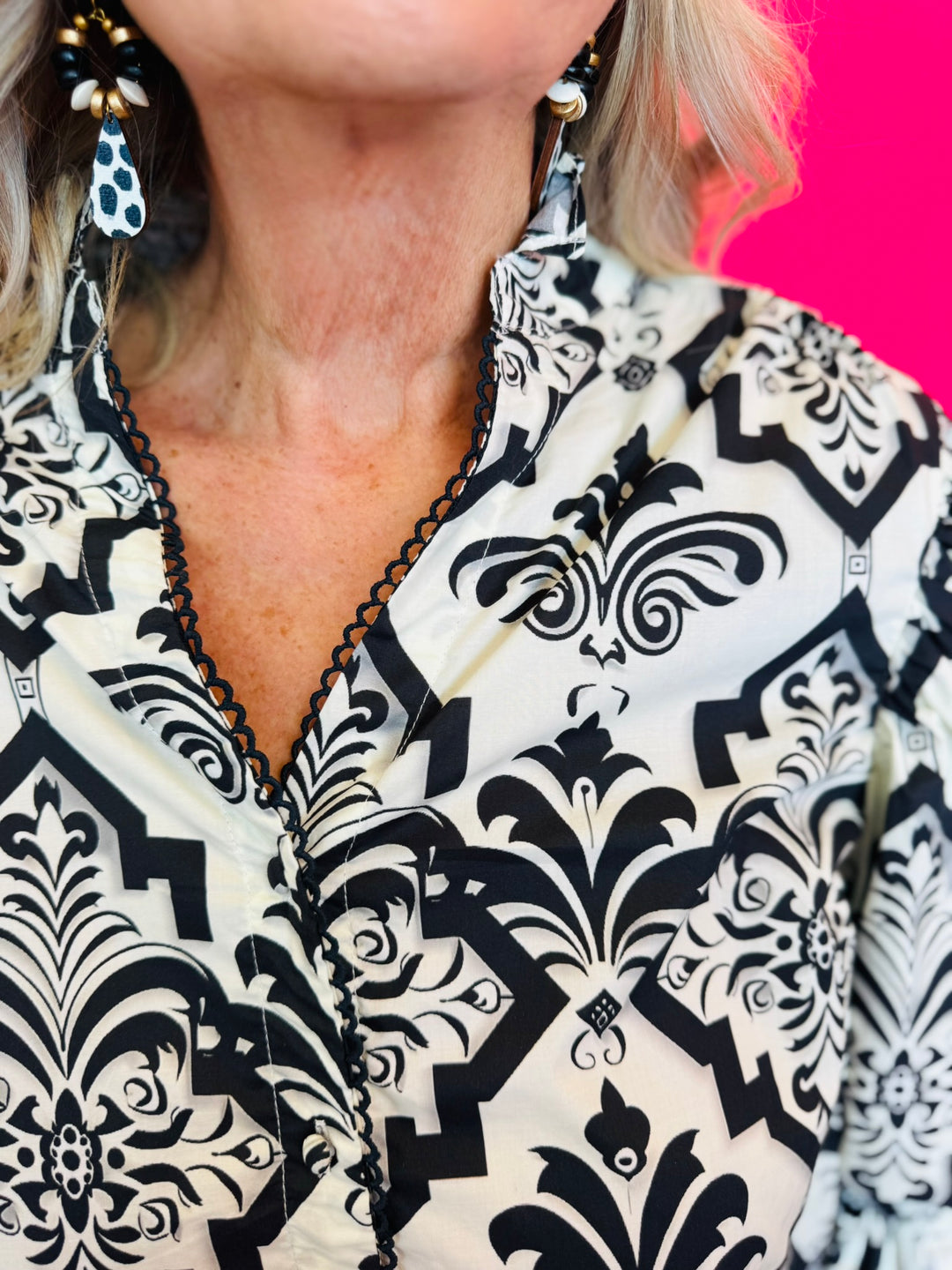 Structured collar and neckline with decorative trim detail against black damask print.
