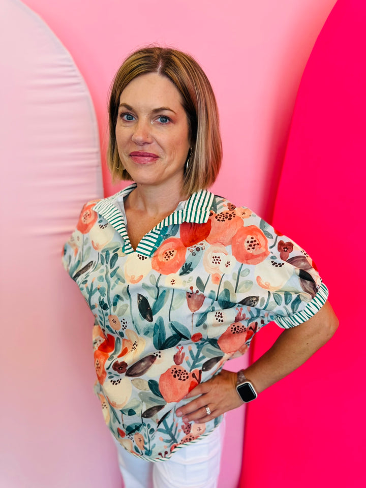 Teal floral mock neck top with coral and peach blooms, striped split neckline with decorative trim, and relaxed short puff sleeves.
