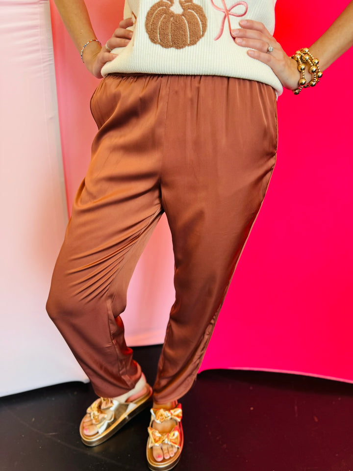 Cinnamon satin jogger-style pants with smocked elastic waistband, relaxed fit, and side pockets.