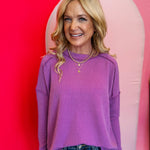 Light plum ribbed boat neck top with raw edge detailing, long sleeves, and relaxed fit.