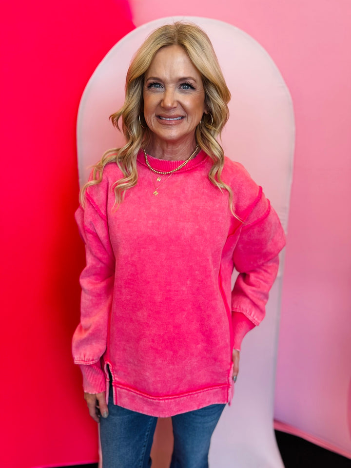 Fuchsia acid wash fleece sweatshirt with exposed seams, relaxed fit, and side slits.
