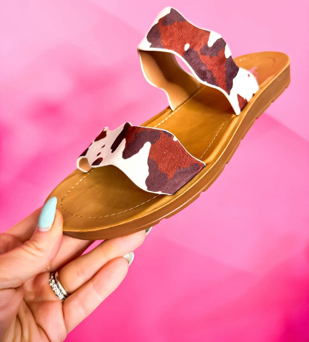 Brown cow print Corkys Wishy Washy sandals featuring playful crisscross straps, cushioned footbed, and a comfortable, modern slip-on design perfect for casual summer wear.