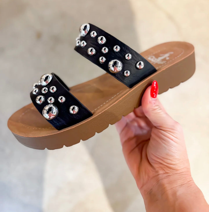 Black embellished double-strap slip-on sandals featuring a cushioned sole and a trendy, versatile design. The straps are adorned with eye-catching details, offering both comfort and style in a sleek silhouette.
