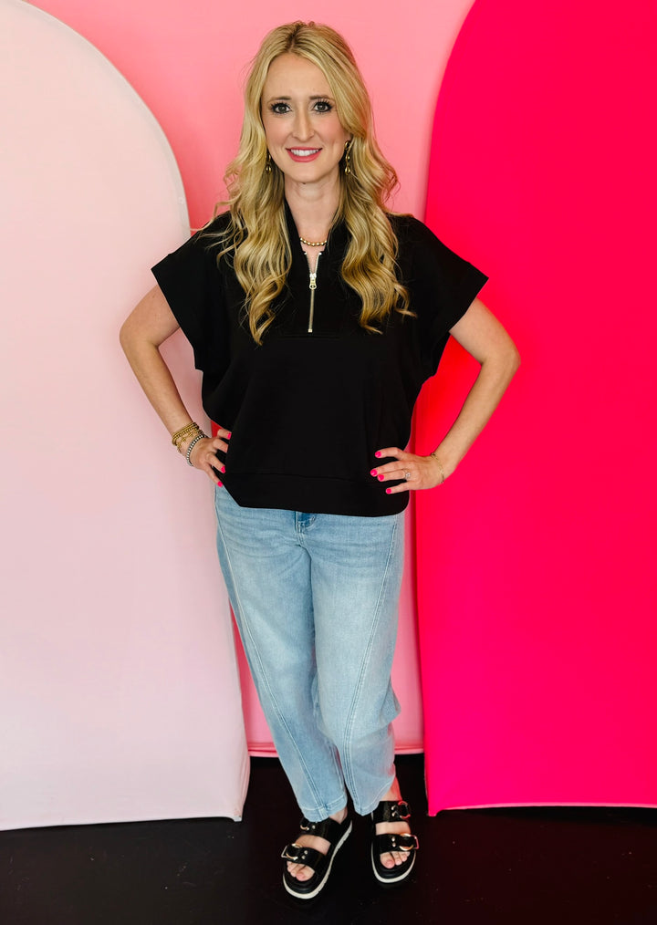 Black scuba high neck top with half zip, displayed folded and styled with denim for a casual-chic look.