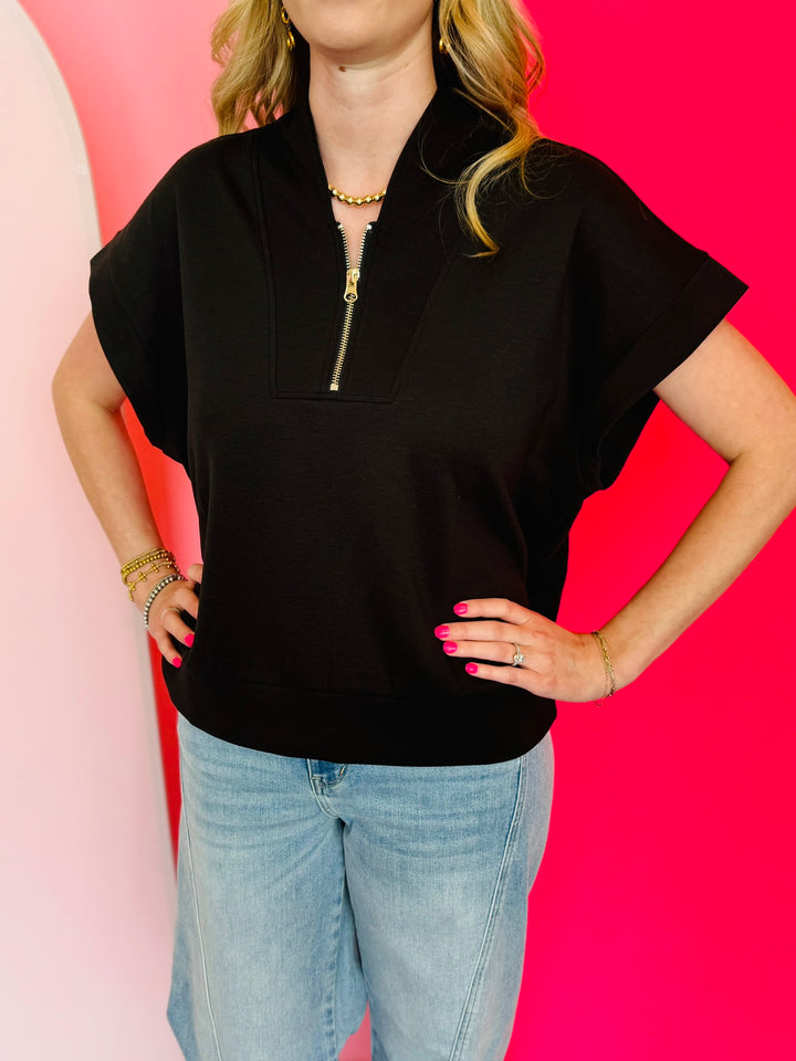 Black scuba high neck top with half zip, displayed folded and styled with denim for a casual-chic look.
