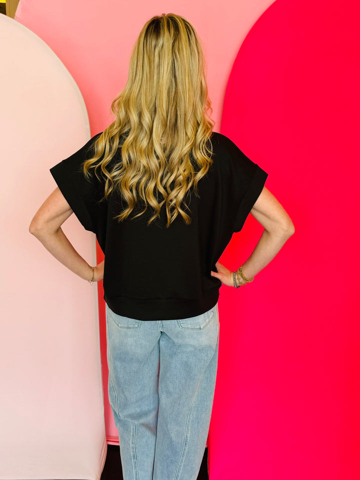 Black scuba high neck top with half zip, displayed folded and styled with denim for a casual-chic look.