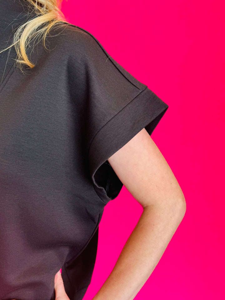 Black scuba high neck top sleeve with half zip, displayed folded and styled with denim for a casual-chic look.