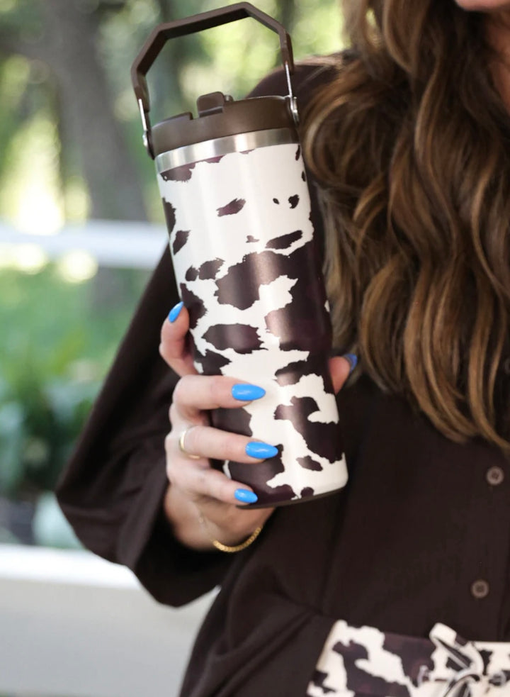30oz chocolate cow print travel tumbler with screw-on lid, handle, and car cup holder–friendly design.