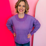 Lavender two-tone sweater with exposed seams, hi-low hem, contrasting trim, and relaxed dropped-shoulder fit.