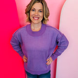 Lavender two-tone sweater with exposed seams, hi-low hem, contrasting trim, and relaxed dropped-shoulder fit.