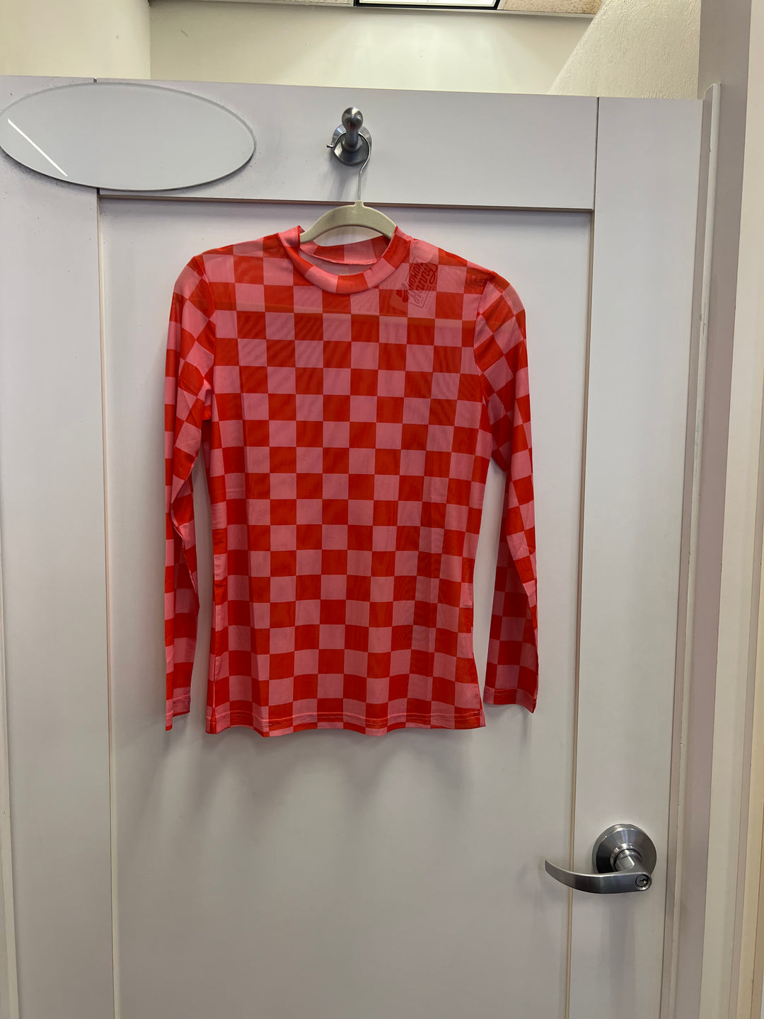 A sheer, long-sleeve mesh top with a mock neckline. The top features a bold, all-over checkerboard pattern in hot pink and red.