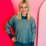 A relaxed-fit, teal and white striped sweater with long sleeves. The sweater has visible exposed seams, a hi-low hemline, and side slits.