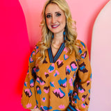 Camel sweater with bright blue, pink, and black leopard spots and striped stand-up V-neck collar.