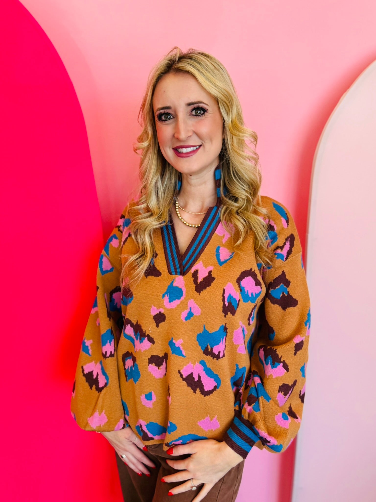 Camel sweater with bright blue, pink, and black leopard spots and striped stand-up V-neck collar.