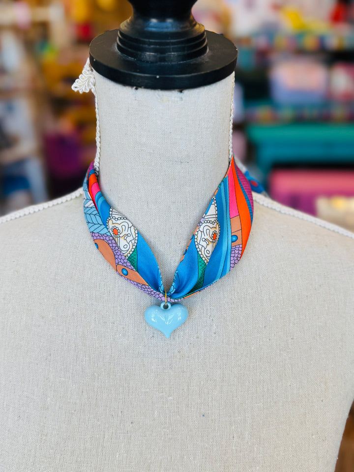 Blue printed scarf necklace featuring a glossy baby blue heart charm; playful and lightweight accessory perfect for adding color and charm to any outfit.