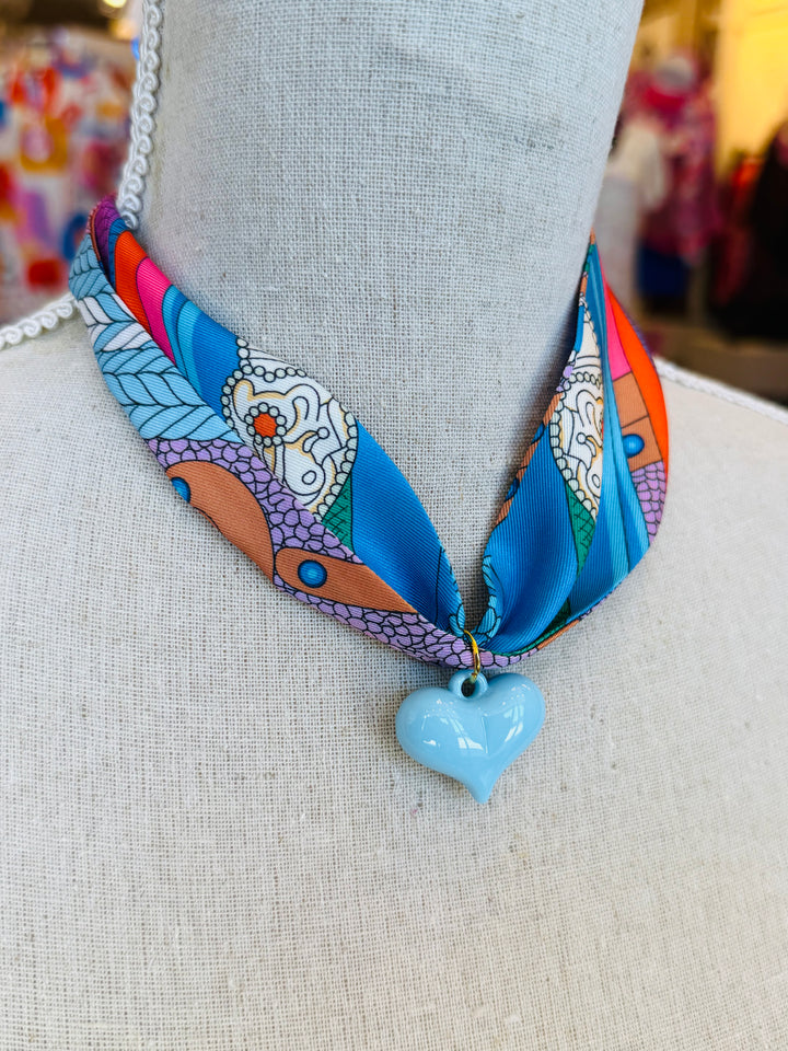 Blue printed scarf necklace featuring a glossy baby blue heart charm; playful and lightweight accessory perfect for adding color and charm to any outfit.