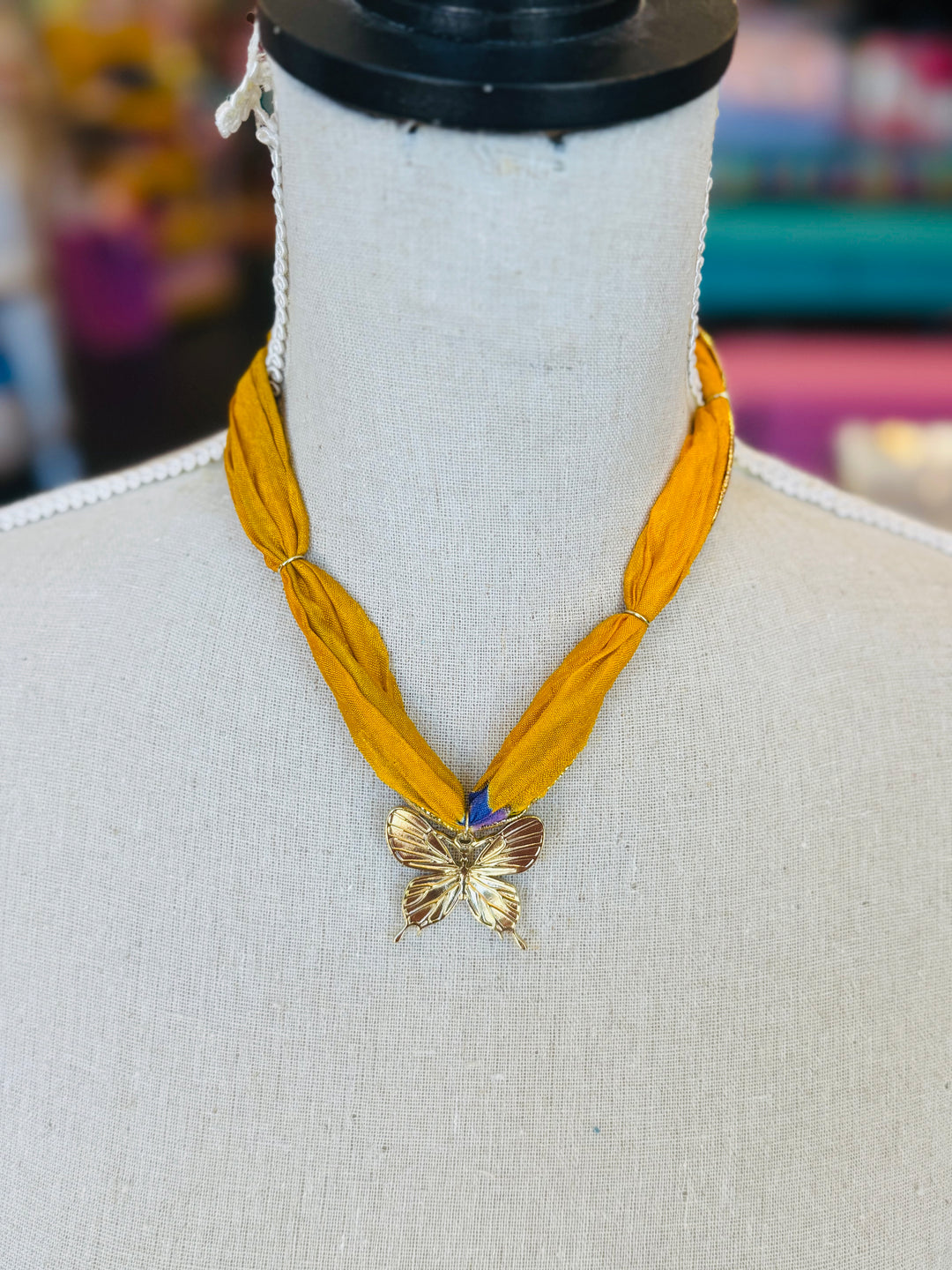 Gold print scarf necklace featuring a delicate gold butterfly charm; a whimsical and stylish accessory perfect for adding elegance and playful charm to any outfit.