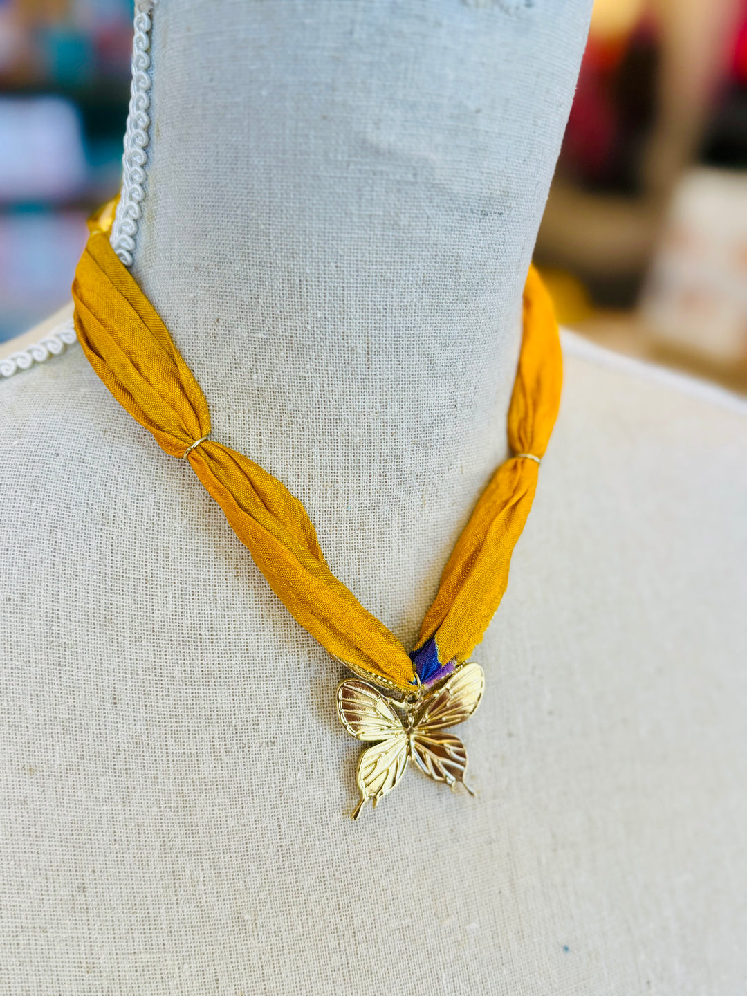 Gold print scarf necklace featuring a delicate gold butterfly charm; a whimsical and stylish accessory perfect for adding elegance and playful charm to any outfit.