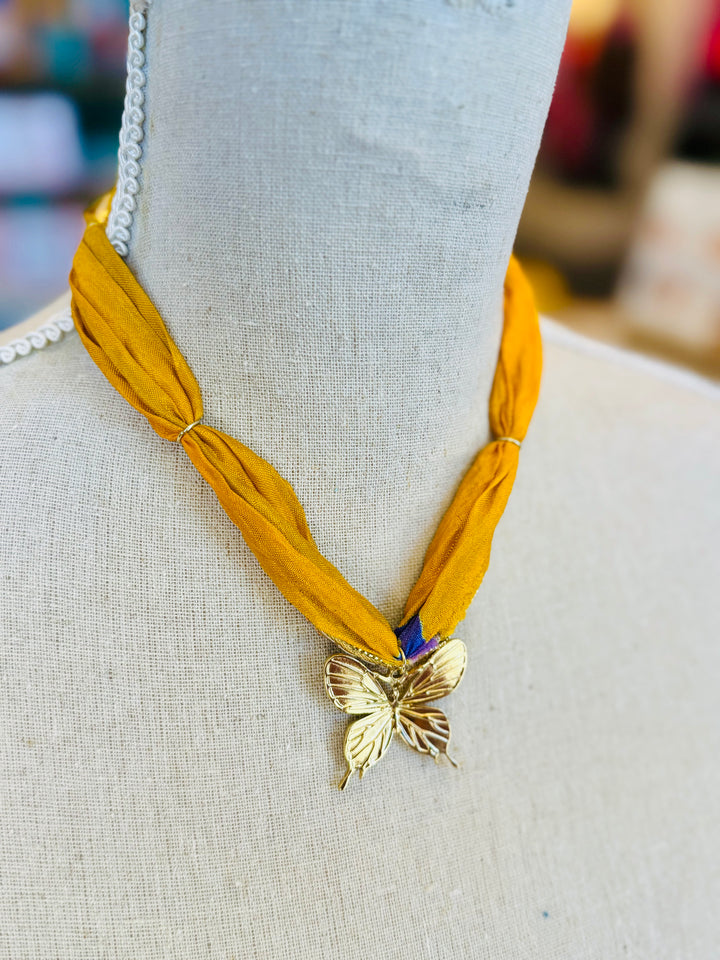 Gold print scarf necklace featuring a delicate gold butterfly charm; a whimsical and stylish accessory perfect for adding elegance and playful charm to any outfit.