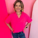 Fuchsia collared V-neck airflow top with short sleeves and a bright, lightweight drape.