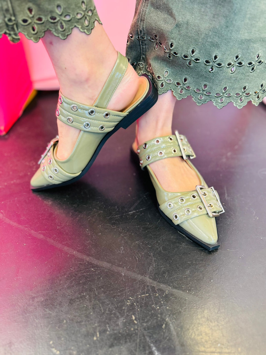 Olive pointed-toe flats with bold silver double buckle straps and a slingback backstrap, combining vibrant color with edgy charm.
