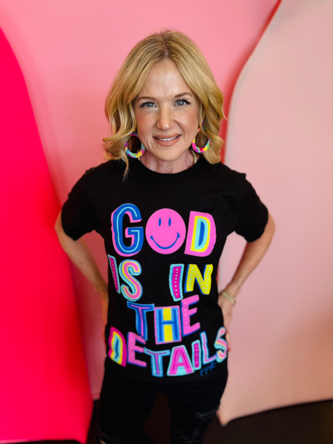 Black graphic tee with "God Is In The Details" in neon colors.