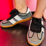 Black rhinestone sneakers with white stripes and gum sole displayed on boutique counter.