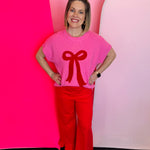 Pink knit sweater with bold textured red bow, crew neckline, and ribbed cuffs.