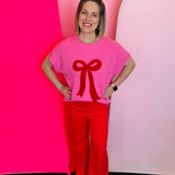 Pink knit sweater with bold textured red bow, crew neckline, and ribbed cuffs.