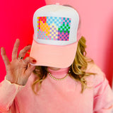 Pink trucker hat with colorful checkerboard graphic and white mesh back.