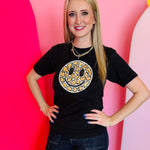 Black Tultex tee with hand-sewn leopard smiley patch worn by smiling woman.