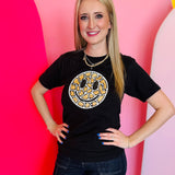 Black Tultex tee with hand-sewn leopard smiley patch worn by smiling woman.
