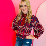 Crimson embroidered eyelet top with ruffled neckline, puff sleeves, and scalloped hem.