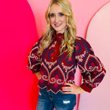 Crimson embroidered eyelet top with ruffled neckline, puff sleeves, and scalloped hem.