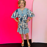 Blue floral babydoll dress with gold print, smocked detail, ruffle hem, and balloon sleeves.