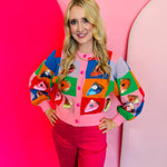 Rainbow colorblock sweater with sequin pie slices, pink buttons, and cropped relaxed fit.