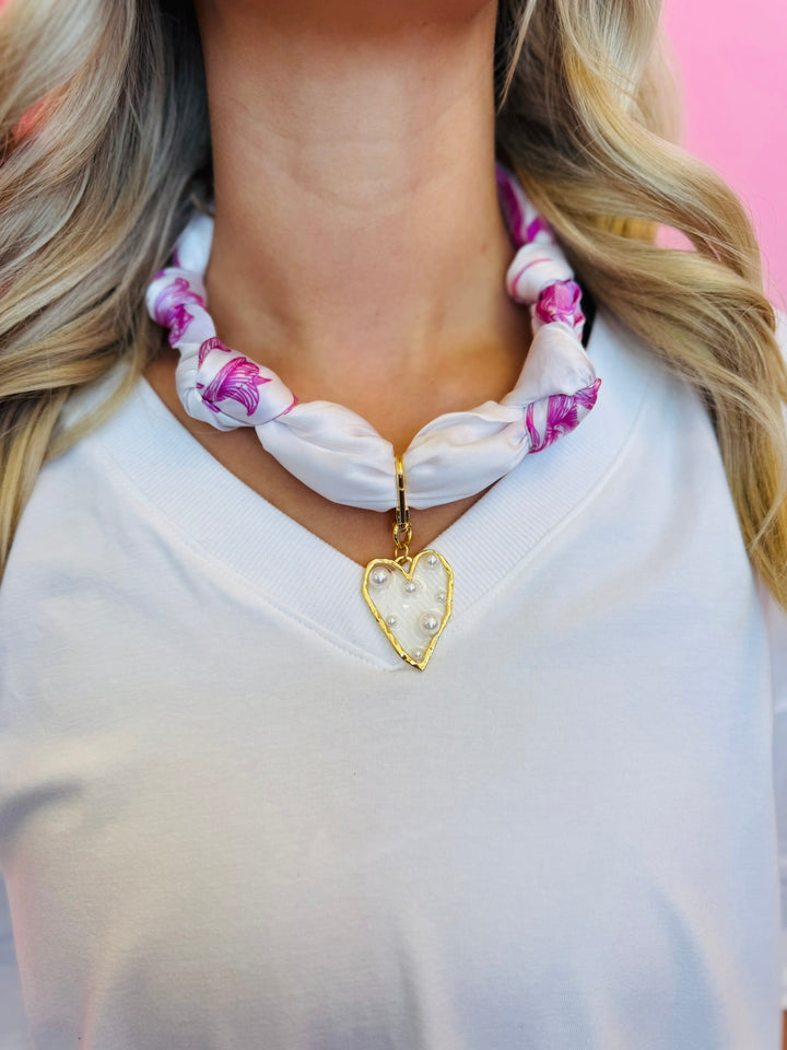 Close-up of the White & Fuchsia silky scarf necklace featuring a gold-trimmed, pearl-embellished heart charm, displayed to highlight color and detail.