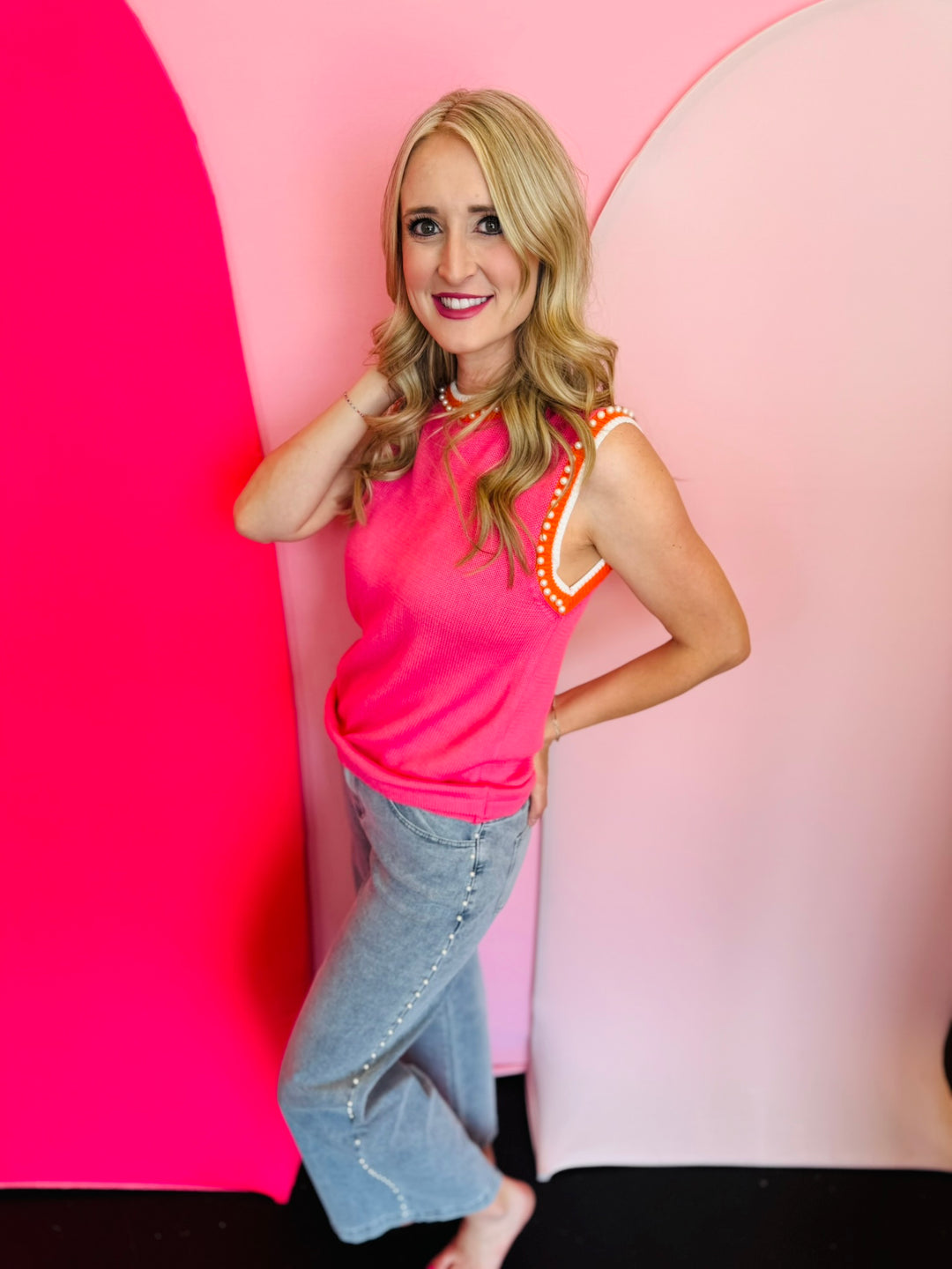 Side profile of the pink sweater vest styled with jeans, showing bold striped trim and relaxed fit.