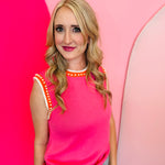 Pink sweater vest with orange and white striped neckline and armholes, worn with jeans; pearl detailing visible on the vest front.