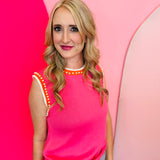 Pink sweater vest with orange and white striped neckline and armholes, worn with jeans; pearl detailing visible on the vest front.